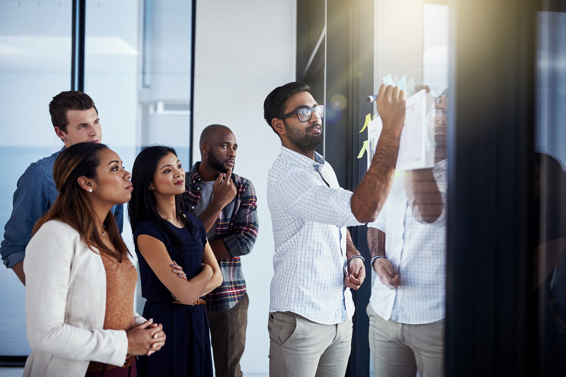 Shot of a young businessman giving a demonstration on a glass wall to his colleagues in a modern office